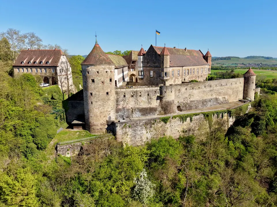 Luftaufnahme des Schlosses Lichtenstein, umgeben von üppigem Grün unter einem strahlend blauen Himmel.